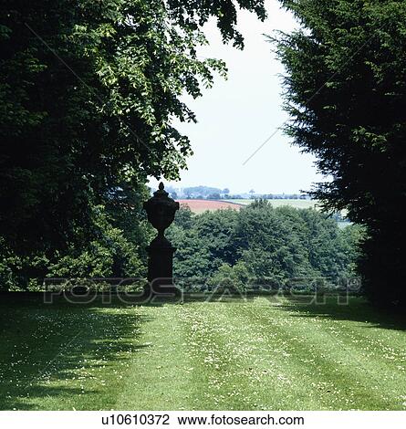 Stock Image - Stone urn on plinth in large country garden in summer. Fotosearch