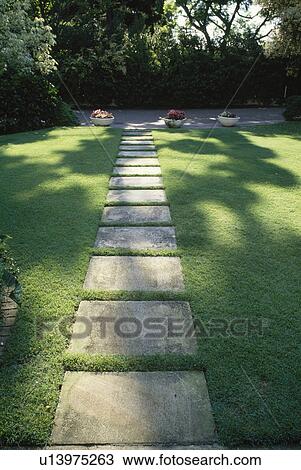 Stock Image - Straight paved path across sunsplashed lawn in country garden. Fotosearch