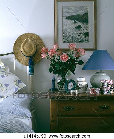 Straw hat on brass bed in bedroom with seascape above blue lamp and pink roses in vase on bedside table View Large Photo Image Stock Photo - Straw hat on brass bed in bedroom with seascape above blue lamp and pink roses in vase on bedside table. Fotosearch