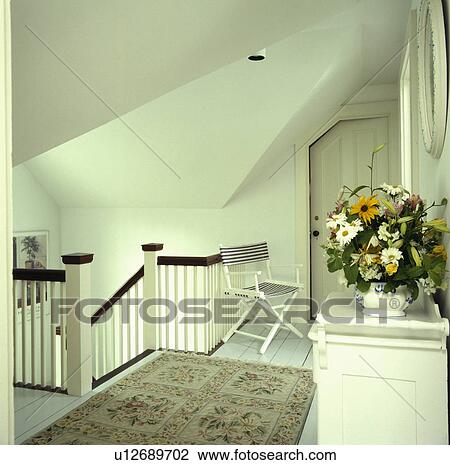 Stock Image - Striped chair and oriental rug on white wooden floor in white attic landing. Fotosearch