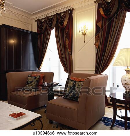 Stock Photograph - Swagged curtains in living room with corner armchairs. Fotosearch