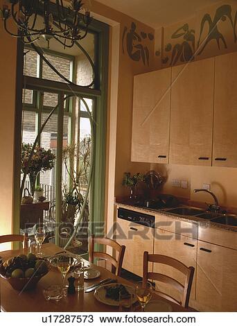 Stock Image - Sycamore wood units in townhouse kitchen dining room with green French doors to the conservatory. Fotosearch