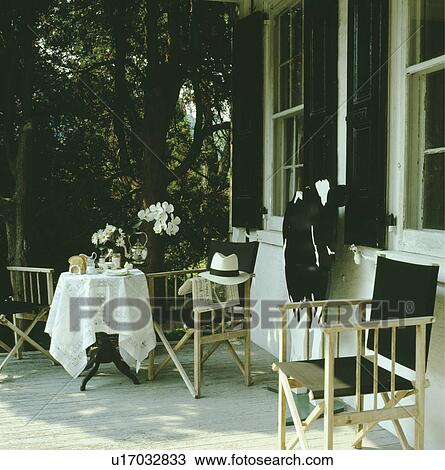 Stock Image - Table and black director's chairs on veranda of traditional house in the country. Fotosearch