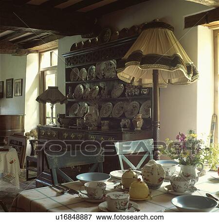 Stock Photo - Table set for breakfast in cottage dining room with standard lamp beside dresser. Fotosearch