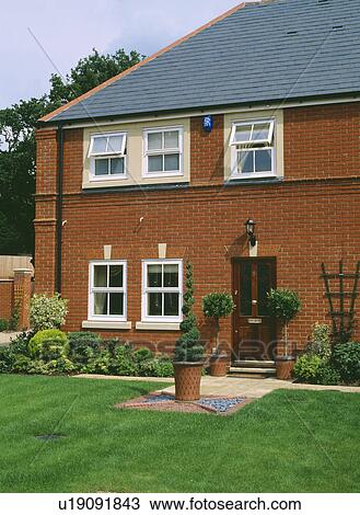 Stock Image - Topiary tree in pot on lawn in front of traditional newbuild house. Fotosearch