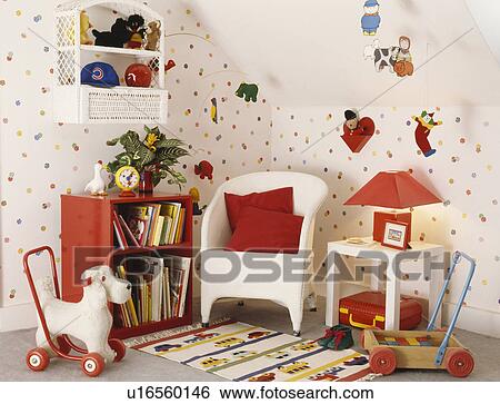 Stock Photograph - Toy dog on wheels and white Lloyd Loom chair with red cushion in children's playroom with spotted wallpaper. Fotosearch