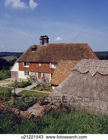 Stock Image - Traditional red brick cottage in the Kent Weald with front garden and adjoining thatched barn. Fotosearch