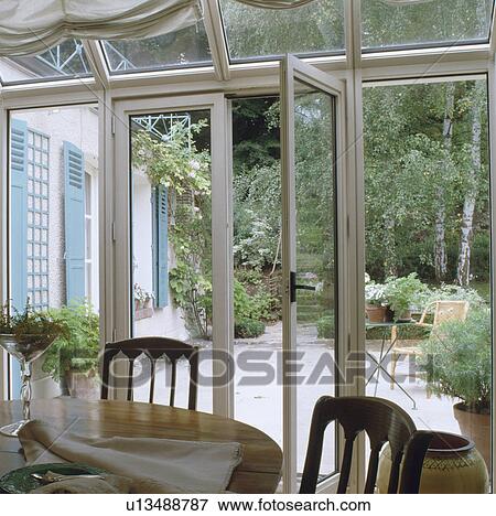 Traditional table and chairs in conservatory extension with view of patio through open glass doors View Large Photo Image Stock Photo - Traditional table and chairs in conservatory extension with view of patio through open glass doors. Fotosearch