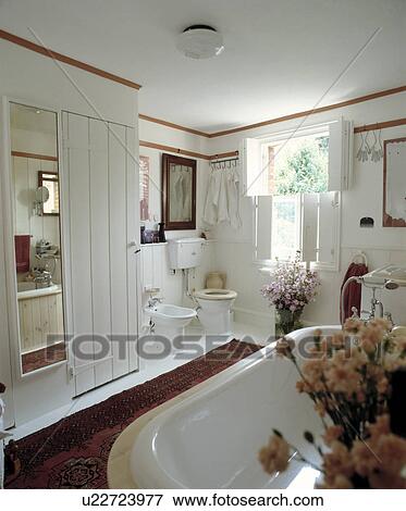 Traditional white bathroom with roll-top bath and shuttered window View Large Photo Image Stock Photo - Traditional white bathroom with roll-top bath and shuttered window. Fotosearch