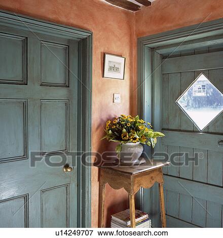 Stock Photo - Turquoise doors with distressed paint effect in terracotta hall with yellow flowers in pot on small wooden table. Fotosearch