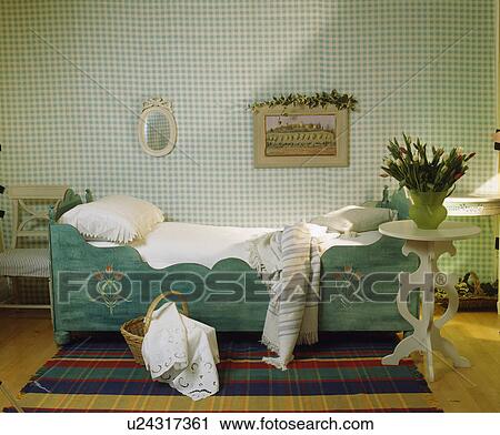 Stock Image - Turquoise green painted wooden child's bed and white table in bedroom with green+white checked wallpaper. Fotosearch