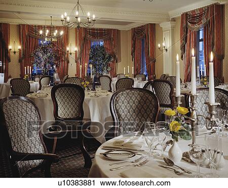 Stock Image - Upholstered chairs and tables with white clothes in hotel dining room with pink curtains. Fotosearch