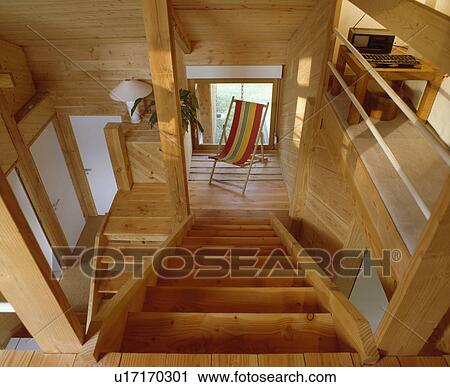 Stock Image - View down wooden staircase to striped deckchair on small wooden landing in openplan wooden hall. Fotosearch