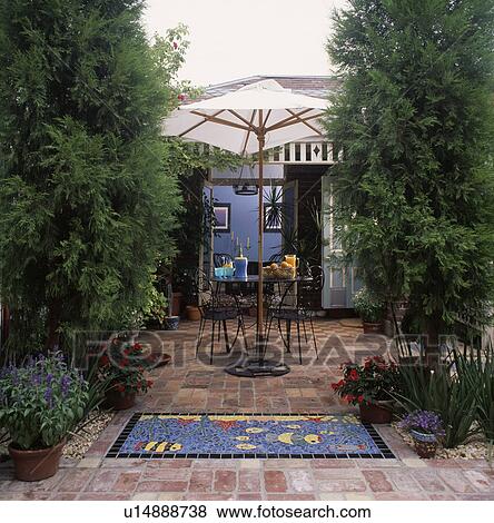 Stock Photo -  View of a brick paved patio with inset undersea mosaic with pots of annuals and shaded with tall conifers&#13; &#10;. Fotosearch