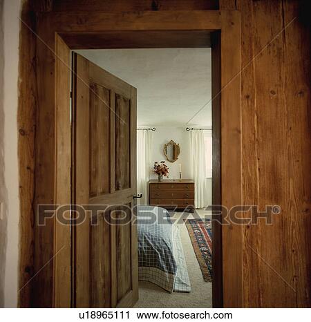 Stock Image - View of traditional bedroom through open old wooden door in panelled wall . Fotosearch