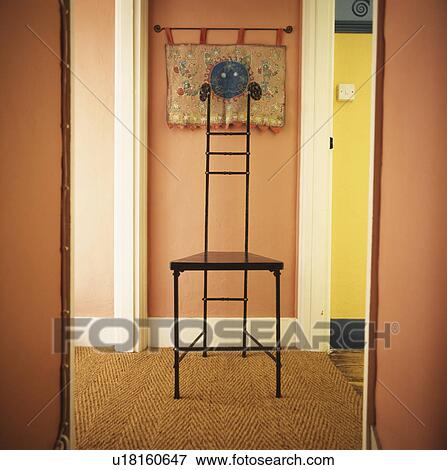 Stock Photo - View through open doorway of tall metal chair in small peach cottage hall with sisal carpet . Fotosearch