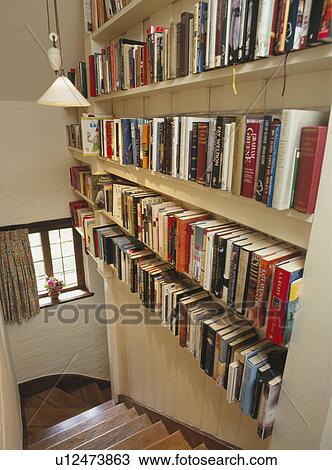 Stock Image - Wall of bookshelves above narrow staircase . Fotosearch
