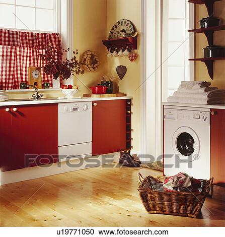 Stock Image - Washing machine and dishwasher in kitchen with red cupboard doors and wooden floors and red+white curtains. Fotosearch