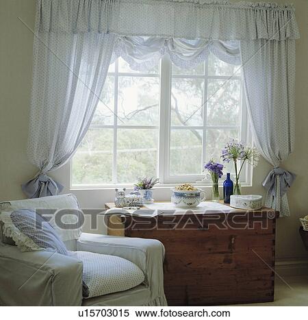 Stock Photography - White armchair beside window with blue spotted voile curtains. Fotosearch