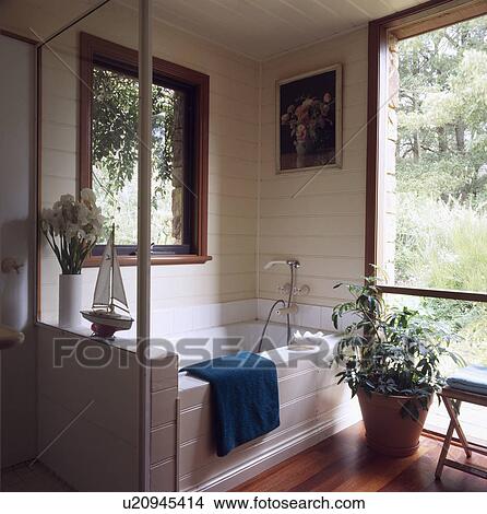 Picture - White bath below window in corner of country bathroom with large houseplant in front of patio door. Fotosearch