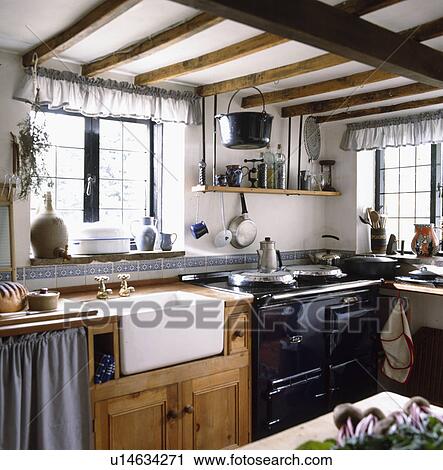 Stock Image - White ceramic sink and black Aga in cottage kitchen. Fotosearch