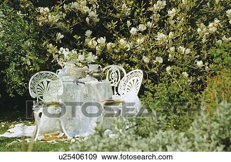 Stock Photo - White chairs and cloth on table in country garden in summer. Fotosearch