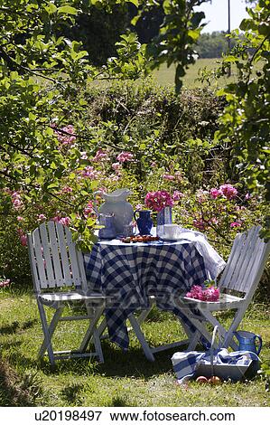 White chairs and table with blue+white checked cloth in country garden in summer View Large Photo Image Stock Photo - White chairs and table with blue+white checked cloth in country garden in summer. Fotosearch