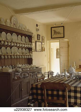 Stock Photo - White china on antique wooden dresser in cream country kitchen with black+white checked cloth on table. Fotosearch