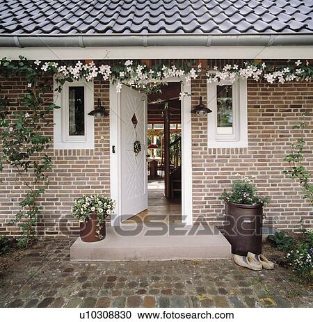 Stock Image - White clematis above open front door on single-storey brick house. Fotosearch
