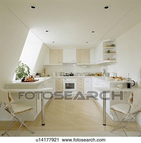 Stock Image - White cushions on metal chairs at breakfast bars in modern white kitchen with wooden floor in attic apartment. Fotosearch