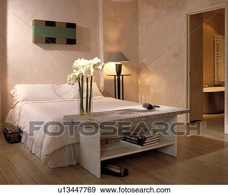 White flowers in glass vase on granite-topped shelves below bed in modern bedroom with textured walls View Large Photo Image Stock Photo - White flowers in glass vase on granite-topped shelves below bed in modern bedroom with textured walls. Fotosearch
