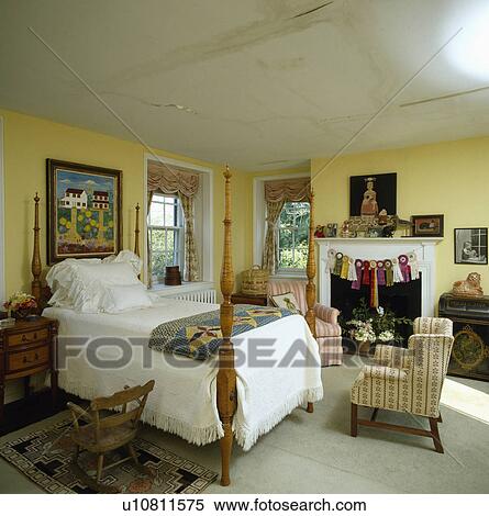 Stock Photography - White linen on bed with turned posts in yellow country bedroom with damp-damaged ceiling. Fotosearch