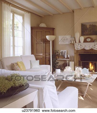 Stock Image - White loosecovers on armchairs in traditional country living room. Fotosearch