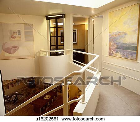 Stock Image - White metal handrail on landing wall with large pictures on walls . Fotosearch