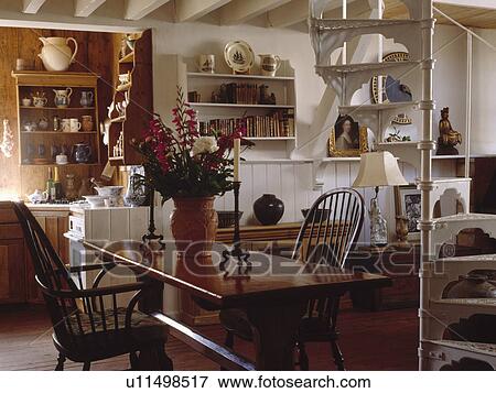 Stock Photo - White metal spiral staircase in openplan cottage hall dining room. Fotosearch