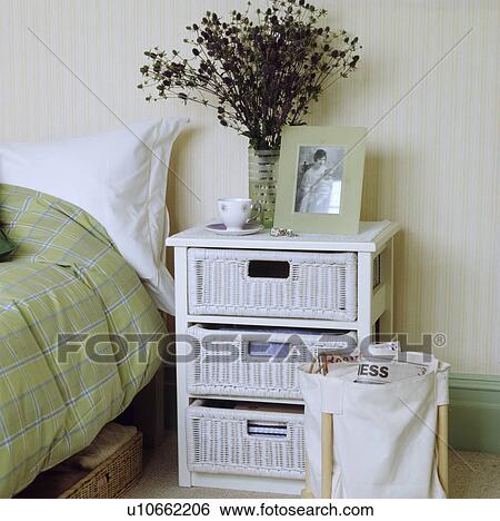Stock Photograph - White painted cane three draw unit in a modern bedroom with pale striped wallpaper. Fotosearch