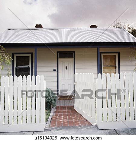 Stock Photography - White picket fence and brick path in front of single-storey traditional white country cottage. Fotosearch