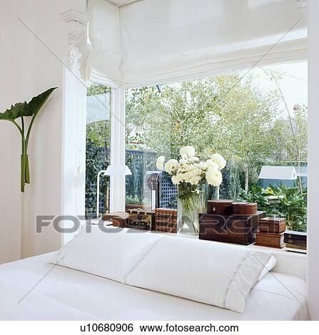 Stock Photograph - White room with bed in front of low window shelf displaying wooden boxes.. Fotosearch