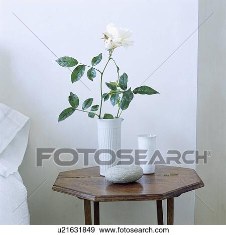 Stock Photo - White rose in a ceramic vase sitting on an octagonal folding dark wood side table . Fotosearch