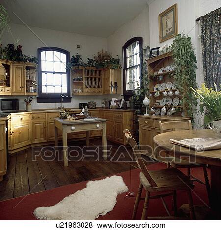 Stock Photo - White sheepskin rug on floor of pine kitchen with pine table and chairs. Fotosearch