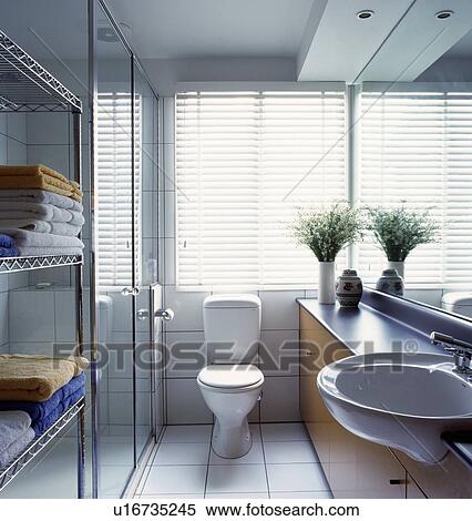 White slatted blind above toilet in small modern white mirrored bathroom with towels on stainless steel shelving View Large Photo Image Stock Photography - White slatted blind above toilet in small modern white mirrored bathroom with towels on stainless steel shelving. Fotosearch