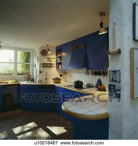 Stock Photo - White tiled worktops and splashbacks in white kitchen with bright blue fitted cupboards. Fotosearch