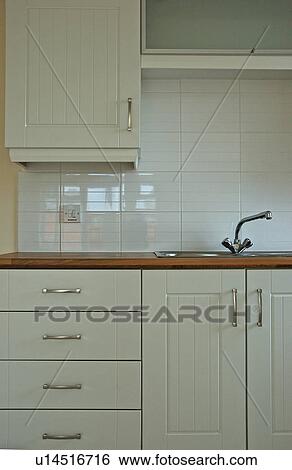 Stock Photograph - White tiles above sink and wooden worktop in modern white kitchen. Fotosearch