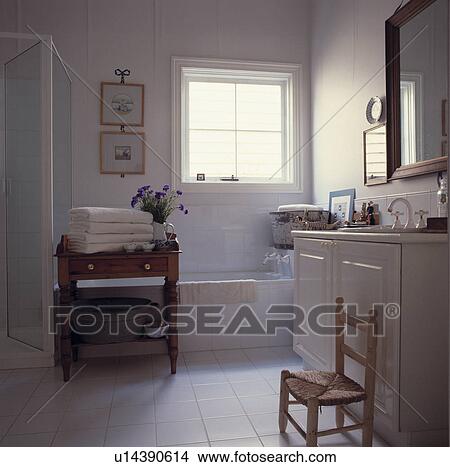 White towels on old pine table in white bathroom with white tiled floor and small Spanish rush-seated chair View Large Photo Image Picture - White towels on old pine table in white bathroom with white tiled floor and small Spanish rush-seated chair. Fotosearch