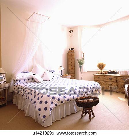 Stock Photography - White voile coronet above bed with blue & white sunburst patterned duvet in bedroom with cream carpet. Fotosearch