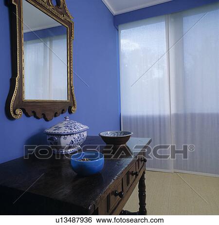 White voile screens in front of windows in bright blue bedroom with gilt mirror above console table View Large Photo Image Stock Photograph - White voile screens in front of windows in bright blue bedroom with gilt mirror above console table. Fotosearch