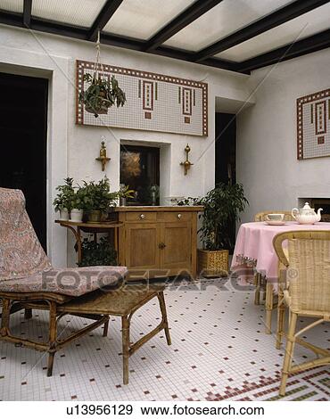 Stock Photo - Wicker chaiselongue in dining room extension with pine cupboard and checked tiled flooring . Fotosearch