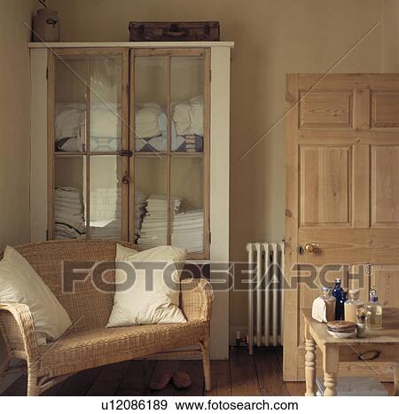 Stock Photo - Wicker sofa and glass-fronted cupboard in neutral bathroom. Fotosearch