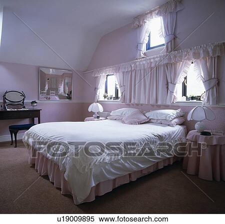 Stock Photography - Windows above bed with white bedlinen in pale mauve attic conversion bedroom. Fotosearch