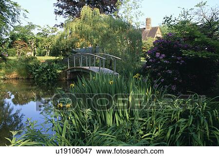 Stock Photo - Wooden footbridge over stream in large country garden. Fotosearch